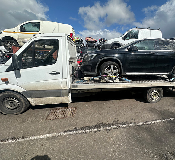 towed vehicle on truck with other cars in background and blue sky displaying three cars on top